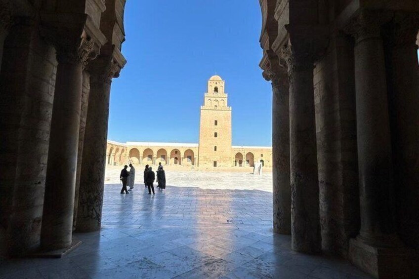 A courtyard with columns, a tower, and people walking. 4