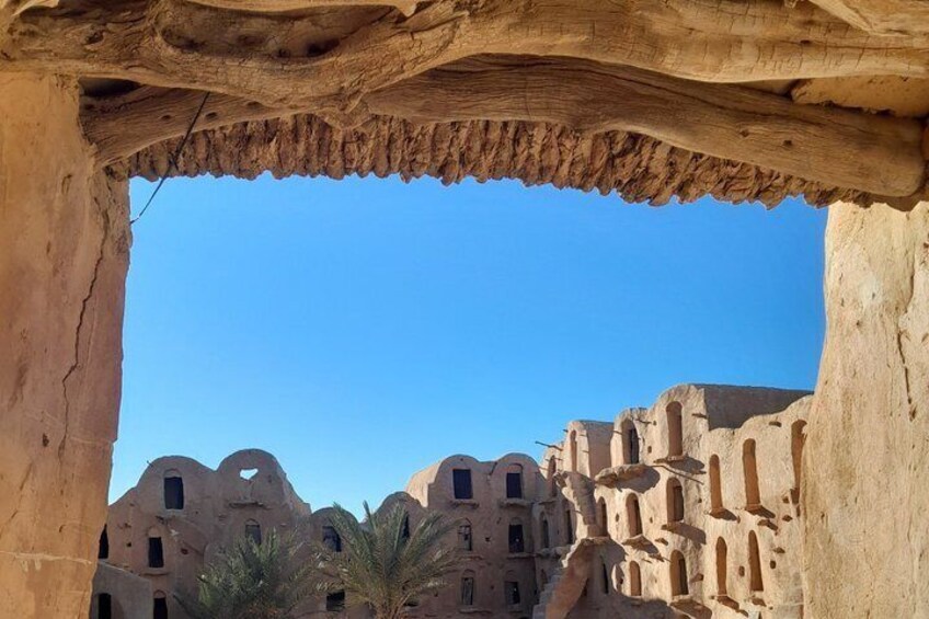 A rock arch framing a view of ancient, multi-story buildings with arched windows and doorways. 1