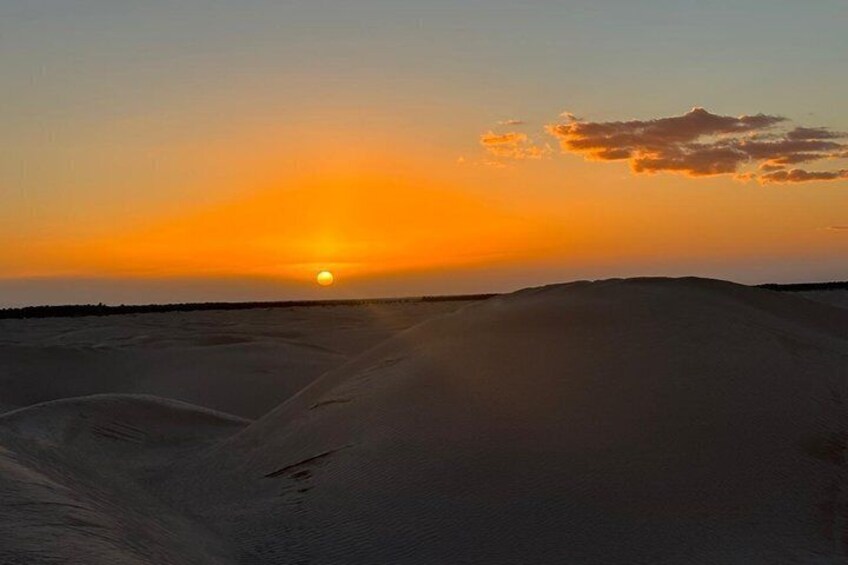 A desert landscape at sunset with a clear sky and a visible sun. 3