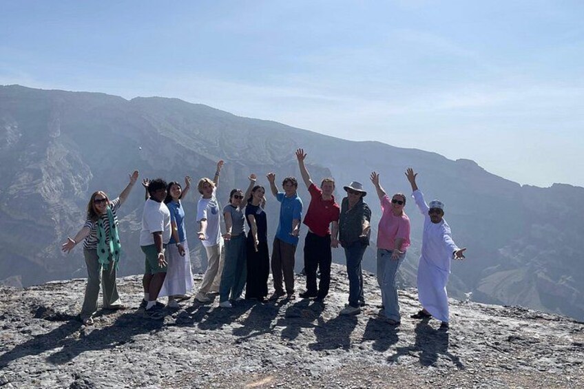 A group of people standing on a rocky outcrop with their arms raised, overlooking a mountainous landscape. 3
