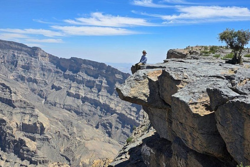 A person sitting on a rock ledge overlooking a canyon with layered rock formations. 1