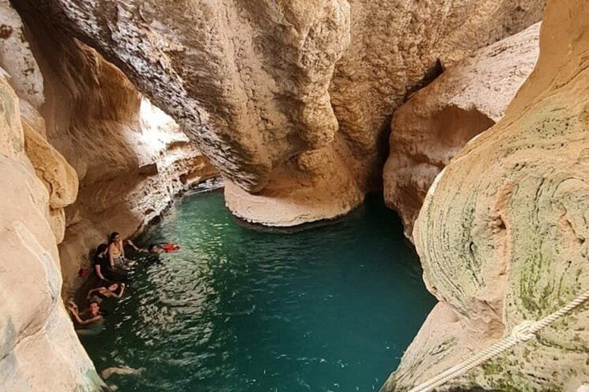 A cave with a turquoise pool and people sitting by the water. 4