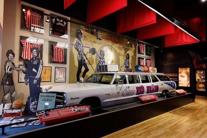 A museum exhibit with a vintage car, sports memorabilia, and a red and white striped backdrop. 3