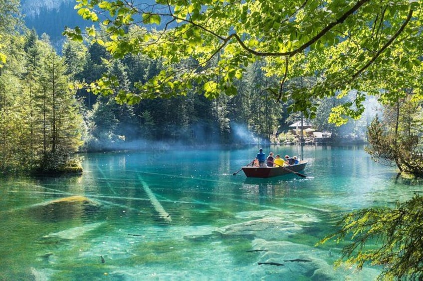 Un lac aux eaux limpides, bordé d’arbres, un bateau avec des personnes à bord et un bâtiment situé au loin. 3