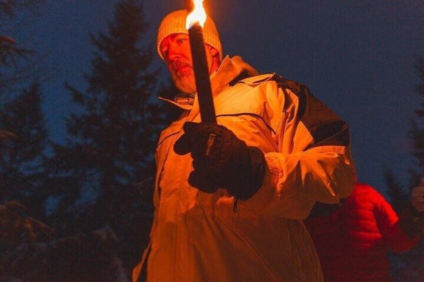A person holding a lit torch in a forested area at night. 2