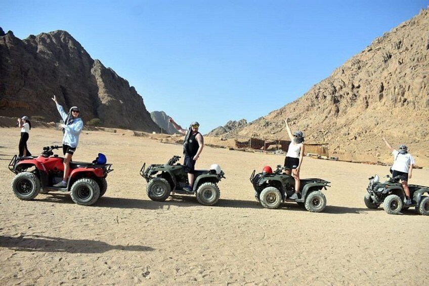 Four people on ATVs in a desert landscape with mountains in the background. 4