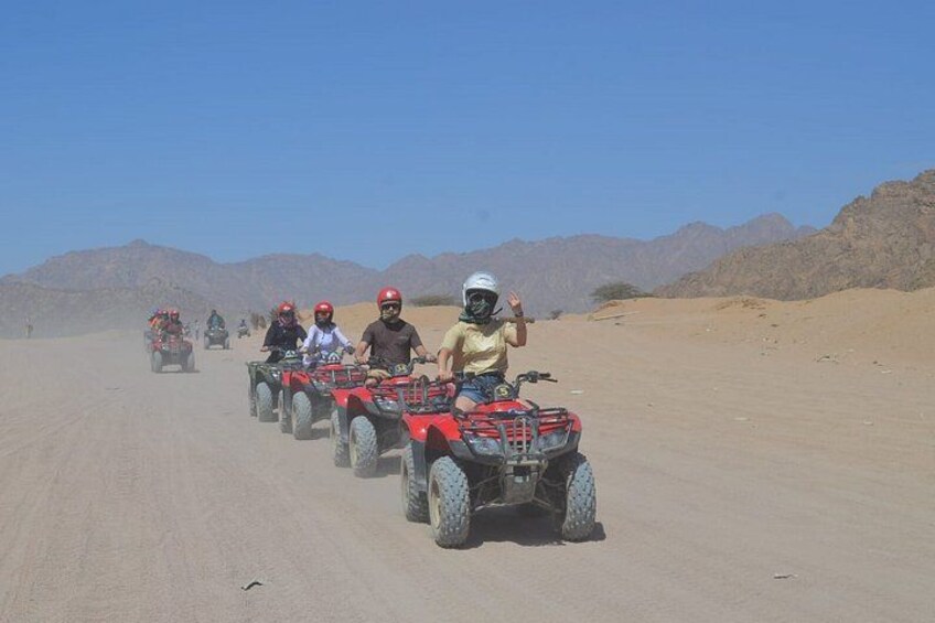 A group of people riding ATVs on a desert road with mountains in the background. 5