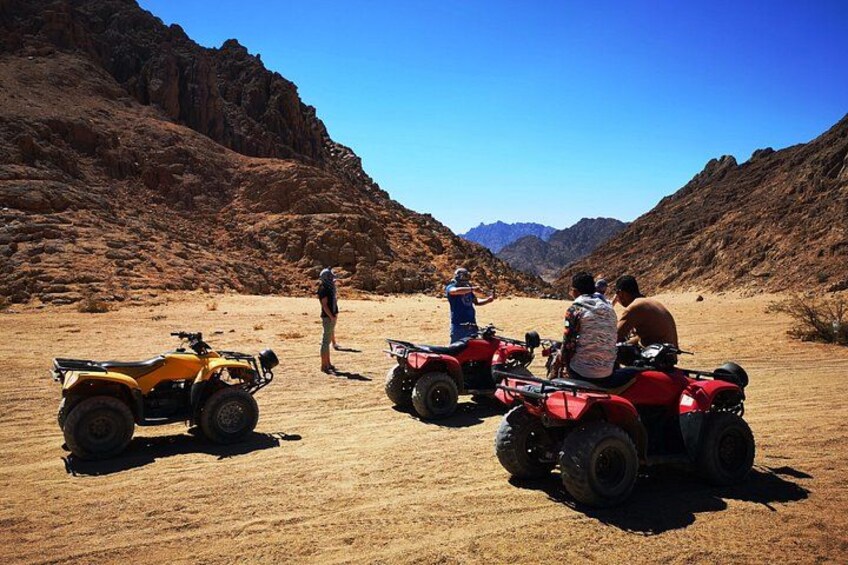 Off-road vehicles in a desert landscape with rocky terrain and mountains in the background. 1