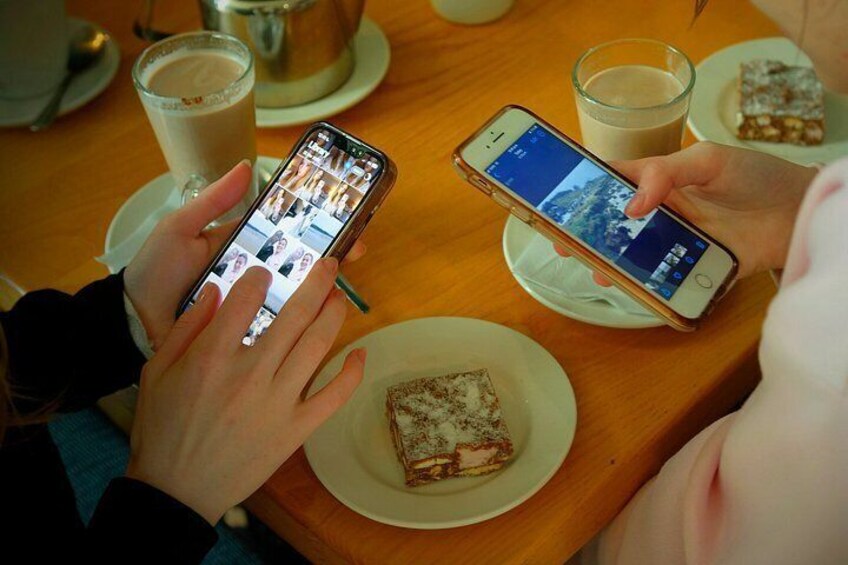 Two people at a table with smartphones, a cup of coffee, and a slice of cake. 3