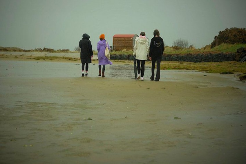 Four people walking on a sandy beach with a wooden structure in the background. 1