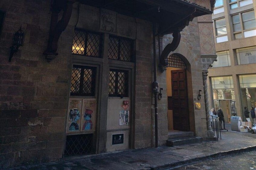 A brick building with a wooden door and windows, a small outdoor seating area, and a paved sidewalk. 4