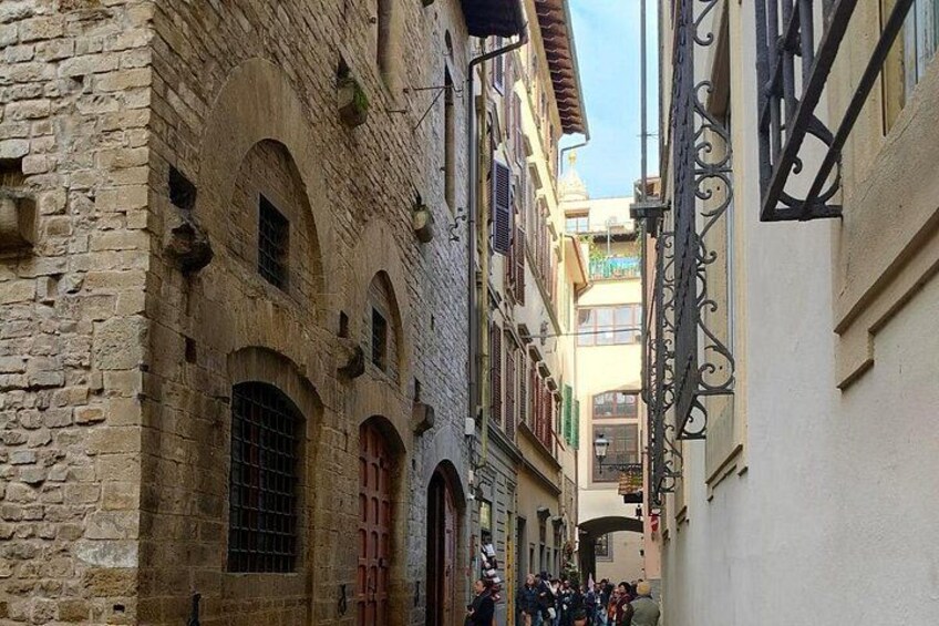 A narrow street with historic stone buildings, arched windows, and a wrought iron gate. 2