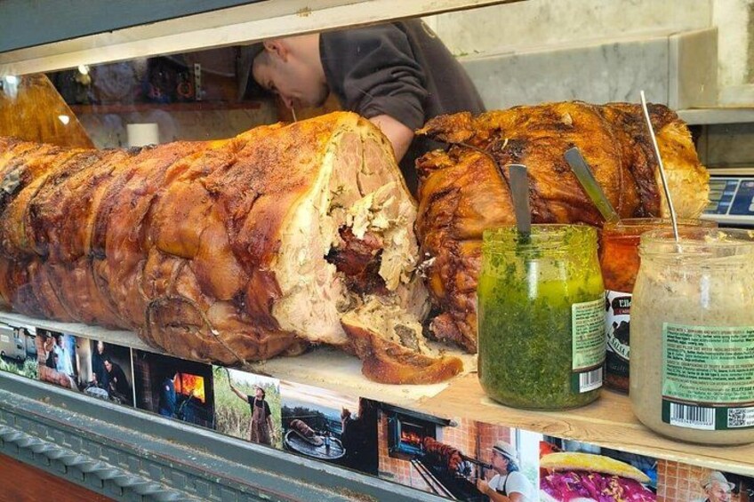 A large roasted pig displayed in a glass case with two jars of condiments. 1