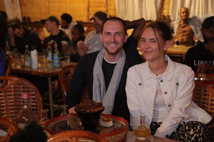 A man and a woman seated at a table with a basket of bread and a bottle of wine. 5