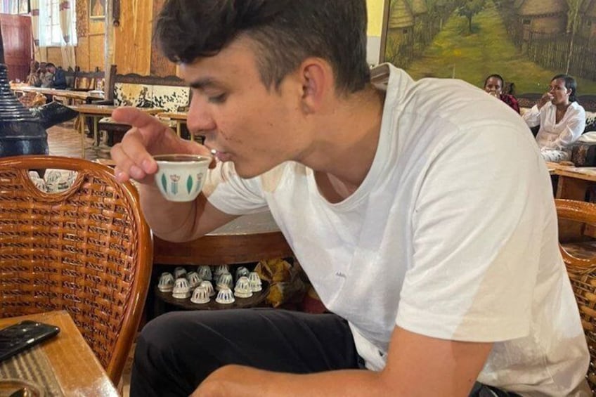 A person sitting at a table in a restaurant, holding a cup. 4