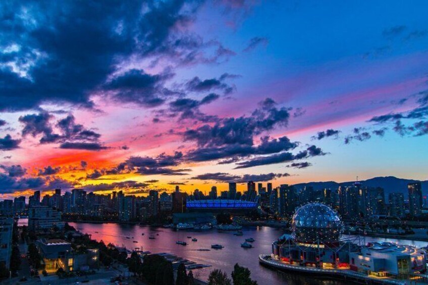 Una skyline cittadina al crepuscolo con un cielo dai colori vivaci, una grande ruota panoramica e un ponte sopra un fiume. 5