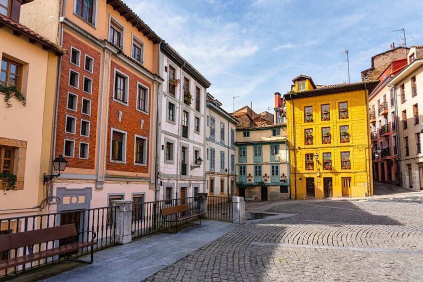Una calle adoquinada flanqueada por edificios de colores, un banco y un cielo azul despejado. 2