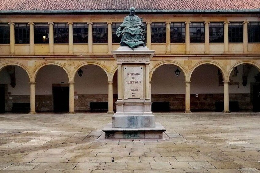 Un patio con una estatua, un edificio con arcos y un tejado de azulejos. 4