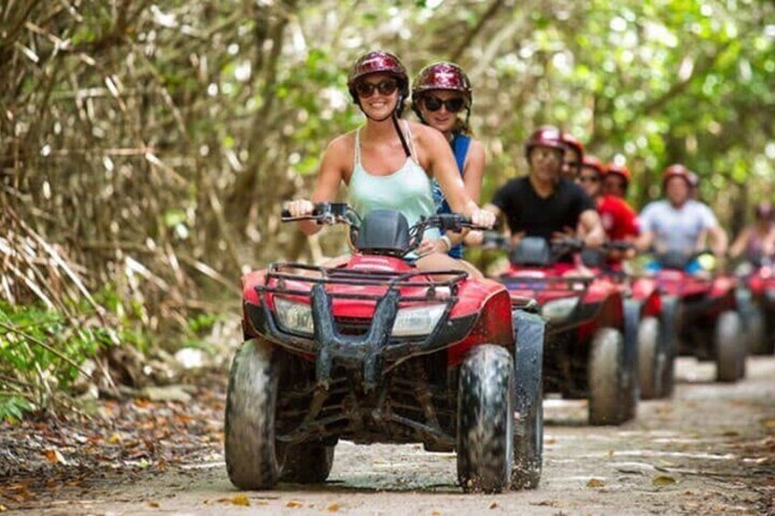 People riding ATVs on a dirt path surrounded by trees. 1