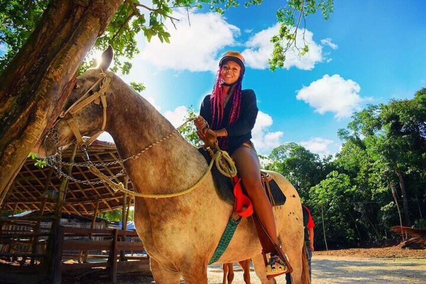 A person riding a horse with a saddle, in a rural setting with trees and a wooden structure in the background. 4