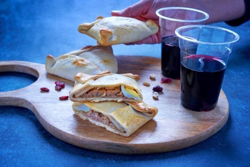 Ein Holzbrett mit einem gefalteten Gebäck, zwei Gläsern dunkler Flüssigkeit und verstreuten Beeren. 5