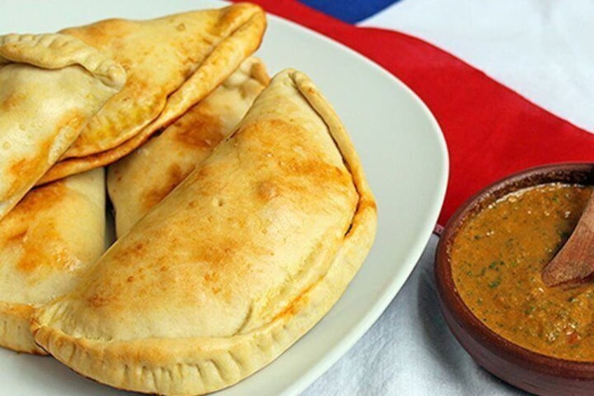 Ein Teller goldbraune Empanadas und eine Schüssel Eintopf mit einem Löffel. 4