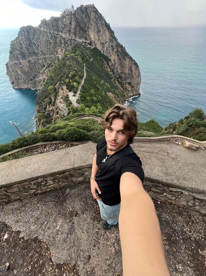 A person taking a selfie with a mountainous landscape and a body of water in the background. 1