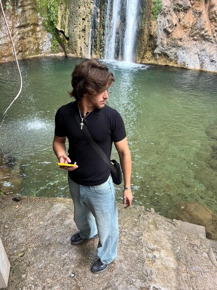 A person standing by a clear water body with a waterfall in the background. 3