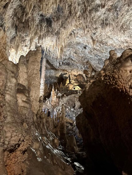 A cave with stalactites and stalagmites, a water stream, and a person standing in the foreground. 2