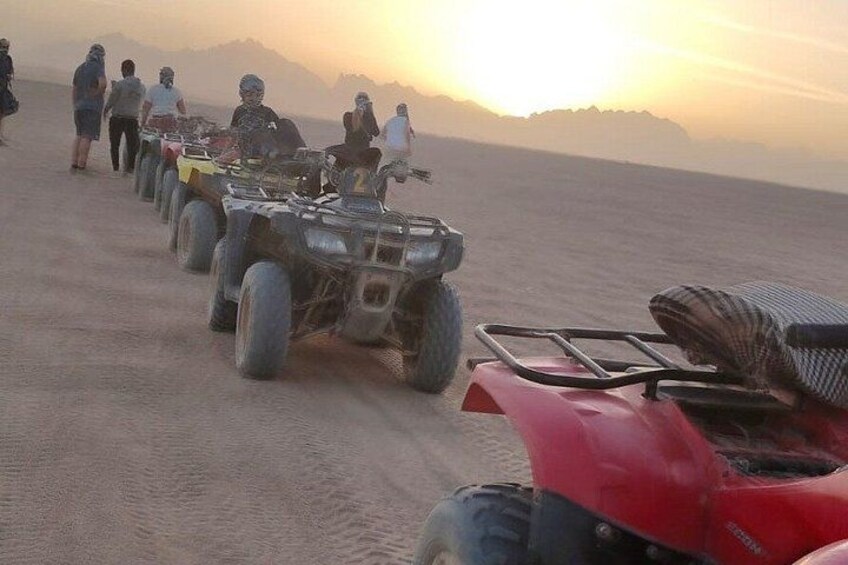 Un groupe de personnes à bord de quads s’est aligné sur une plage de sable, avec le soleil couchant en toile de fond. 5
