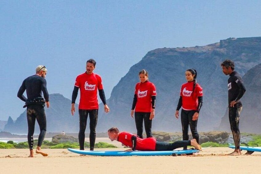 A group of people on a beach with surfboards, mountains in the background, and a person lying on the sand. 5