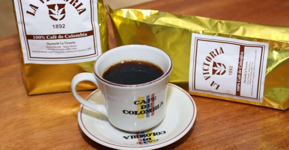 A cup of coffee with a label reading 'CAFE DE COLOMBIA' and two bags of coffee in the background. 3