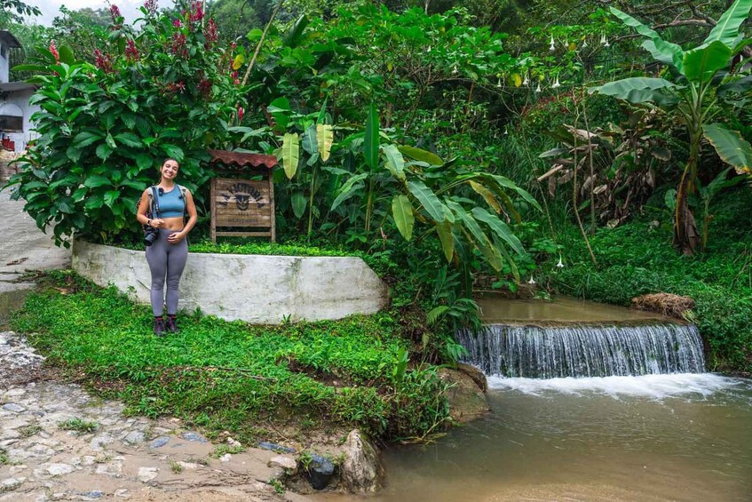 A woman standing by a small waterfall in a lush garden. 1