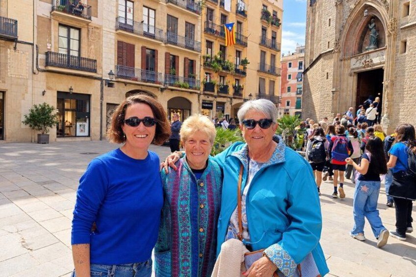 Three people standing in a public square with historic buildings in the background. 1
