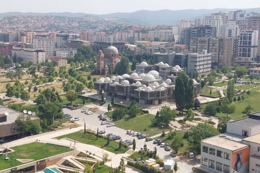 A cityscape with a prominent domed building surrounded by greenery and modern buildings. 1