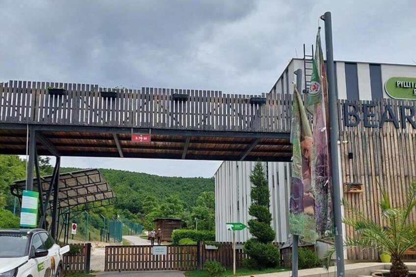 A wooden pedestrian bridge, a sign for 'Pyllyt Barn,' and a parking area with a white car. 3