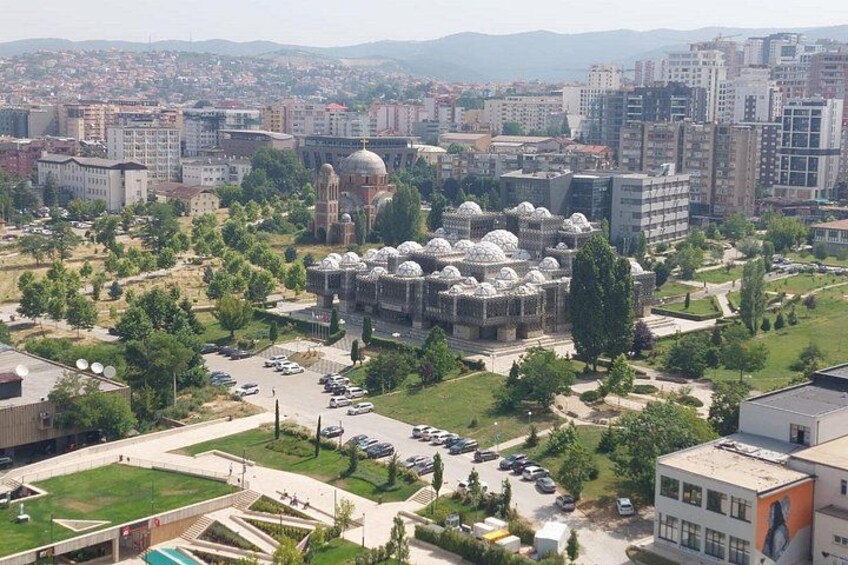 A cityscape with a prominent mosque with multiple domes, surrounded by greenery and modern buildings. 1