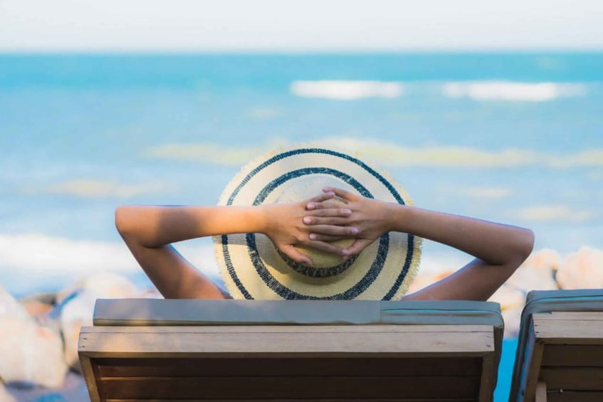 A person sitting on a beach chair with a straw hat, overlooking the ocean. 1