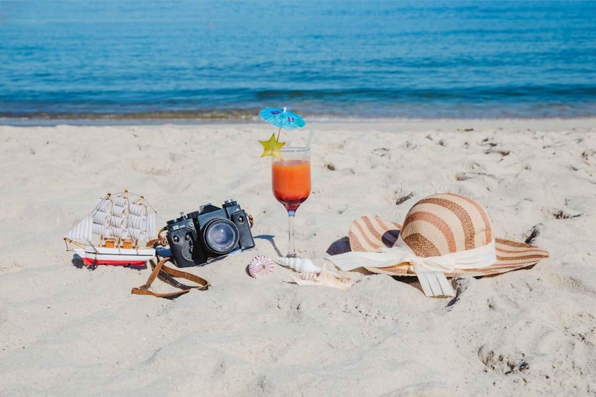 A beach with a camera, a drink, a hat, and a model ship. 4