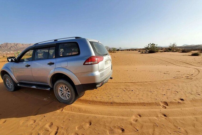 Un SUV plateado estacionado en un camino arenoso del desierto, con huellas que se alejan. 1