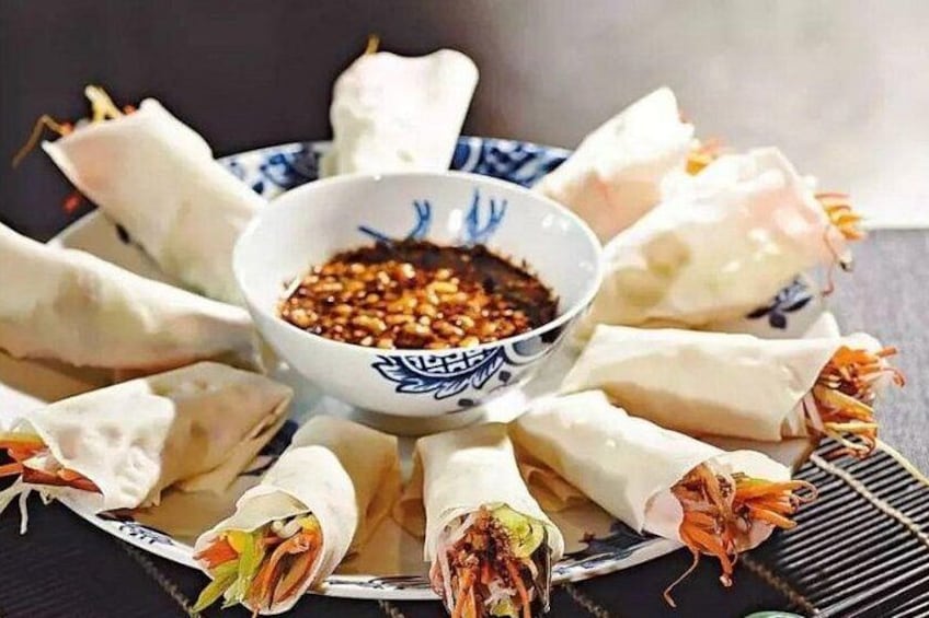 A plate of spring rolls arranged around a bowl of dipping sauce. 5