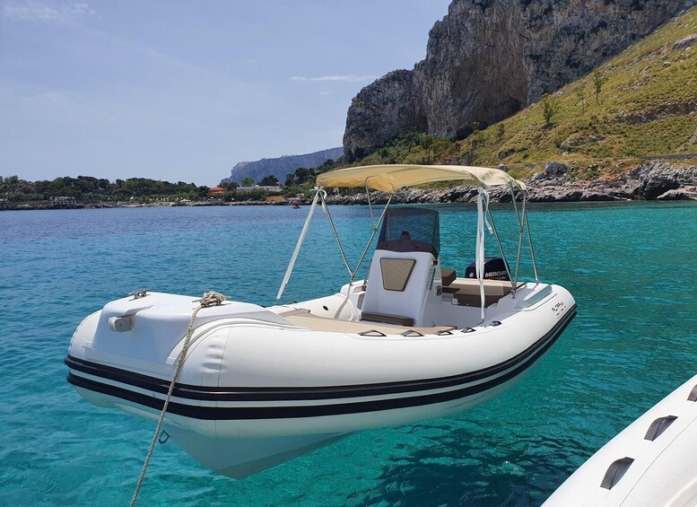 A white inflatable boat with a canopy, anchored in clear turquoise water with a rocky coastline and a cliff in the background. 4