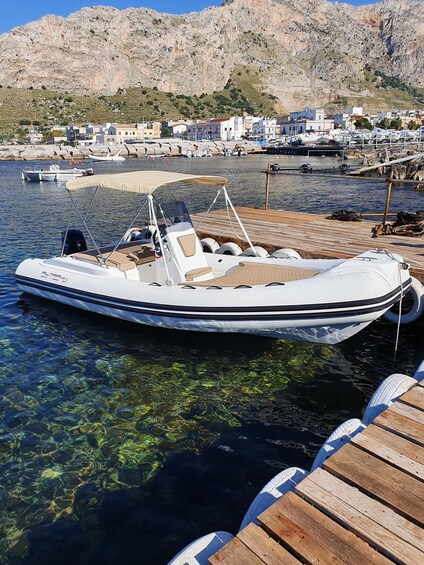 A boat docked at a pier with clear water, rocky hills in the background, and a small town. 1