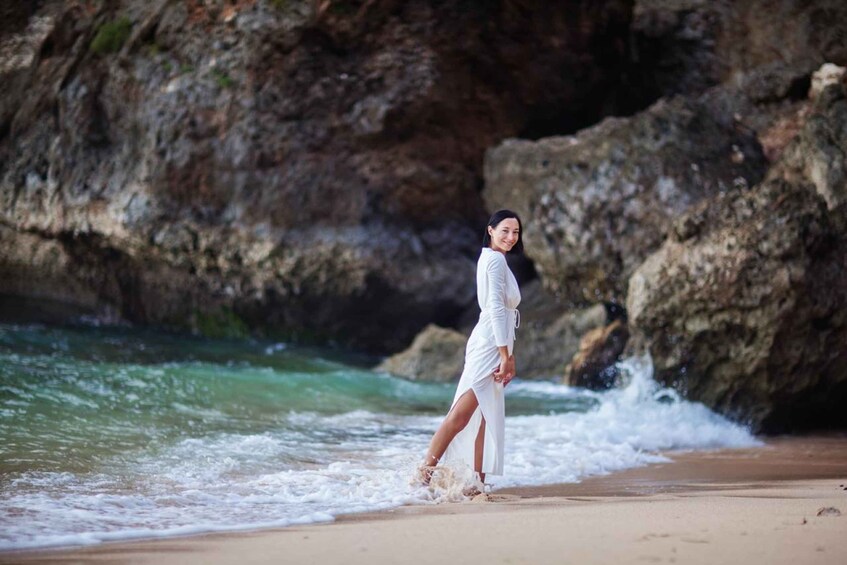 A person in a white dress walking along a rocky beach with waves crashing nearby. 3