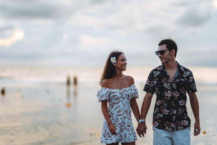 A couple walking on a beach with a cloudy sky. 1