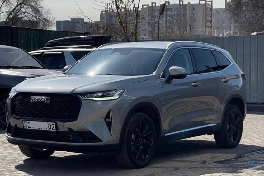Un SUV plateado estacionado en un estacionamiento con edificios al fondo. 2