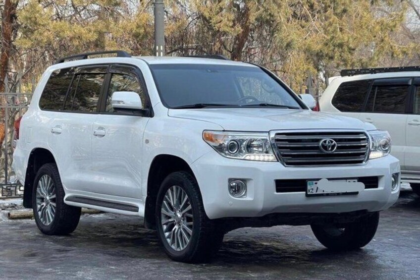 Un SUV blanco estacionado sobre una superficie húmeda, con árboles al fondo. 3