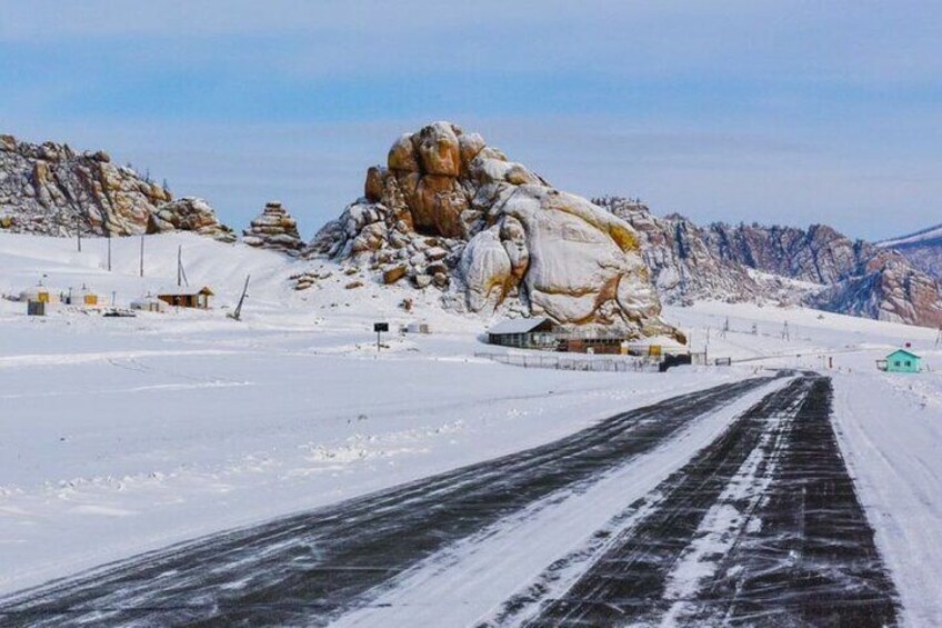 Paisaje nevado con una gran formación rocosa y una carretera pavimentada. 4