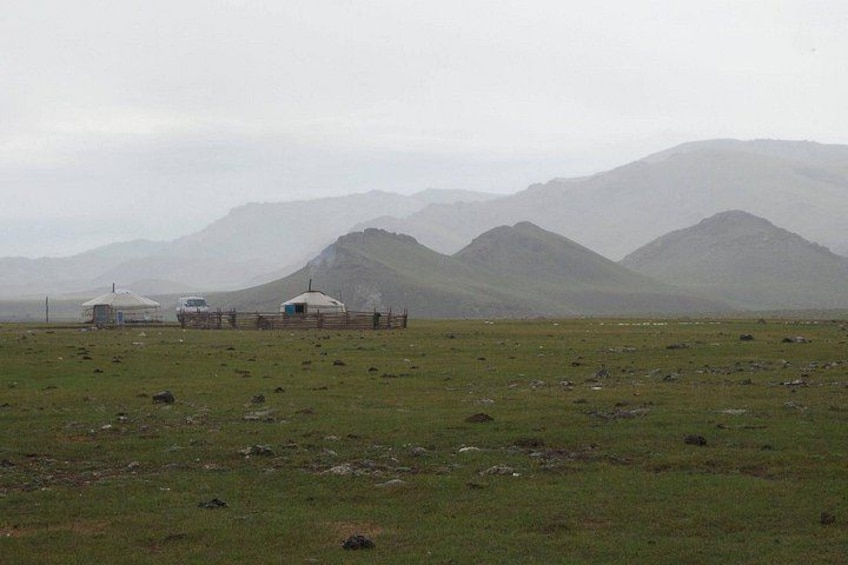 A grassy field with yurts and a mountainous backdrop. 2
