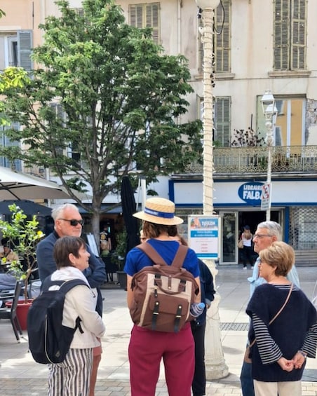 A group of people standing on a sidewalk, a tree, and a building with a sign that reads 'LIBRAIRIE FALB.' 3